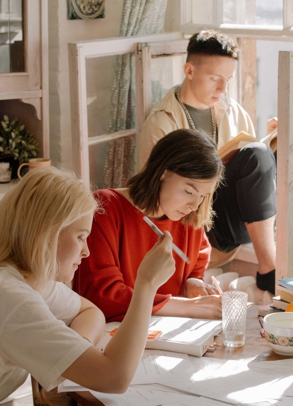 Trois personnes étudient ensemble autour d'une table couverte de livres et de cahiers.